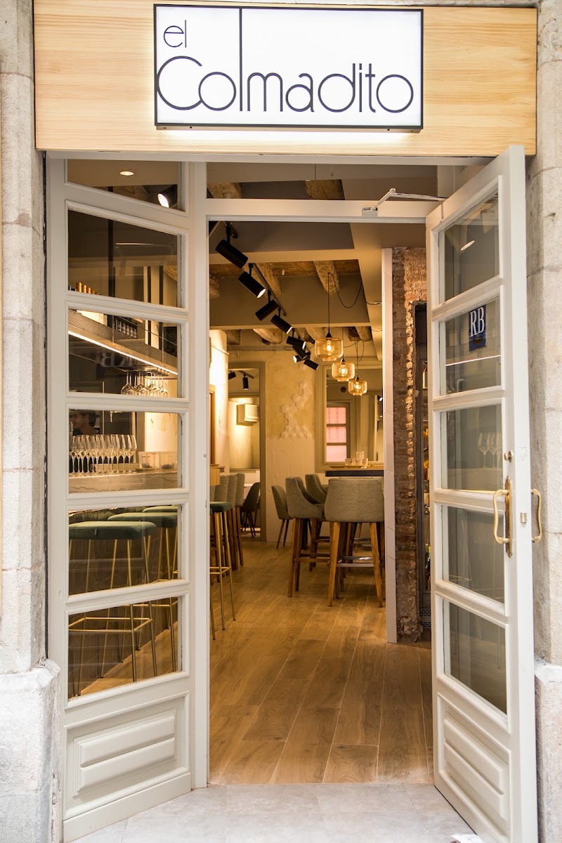 Entrada del restaurante con puertas blancas de cristal y letrero El Colmadito