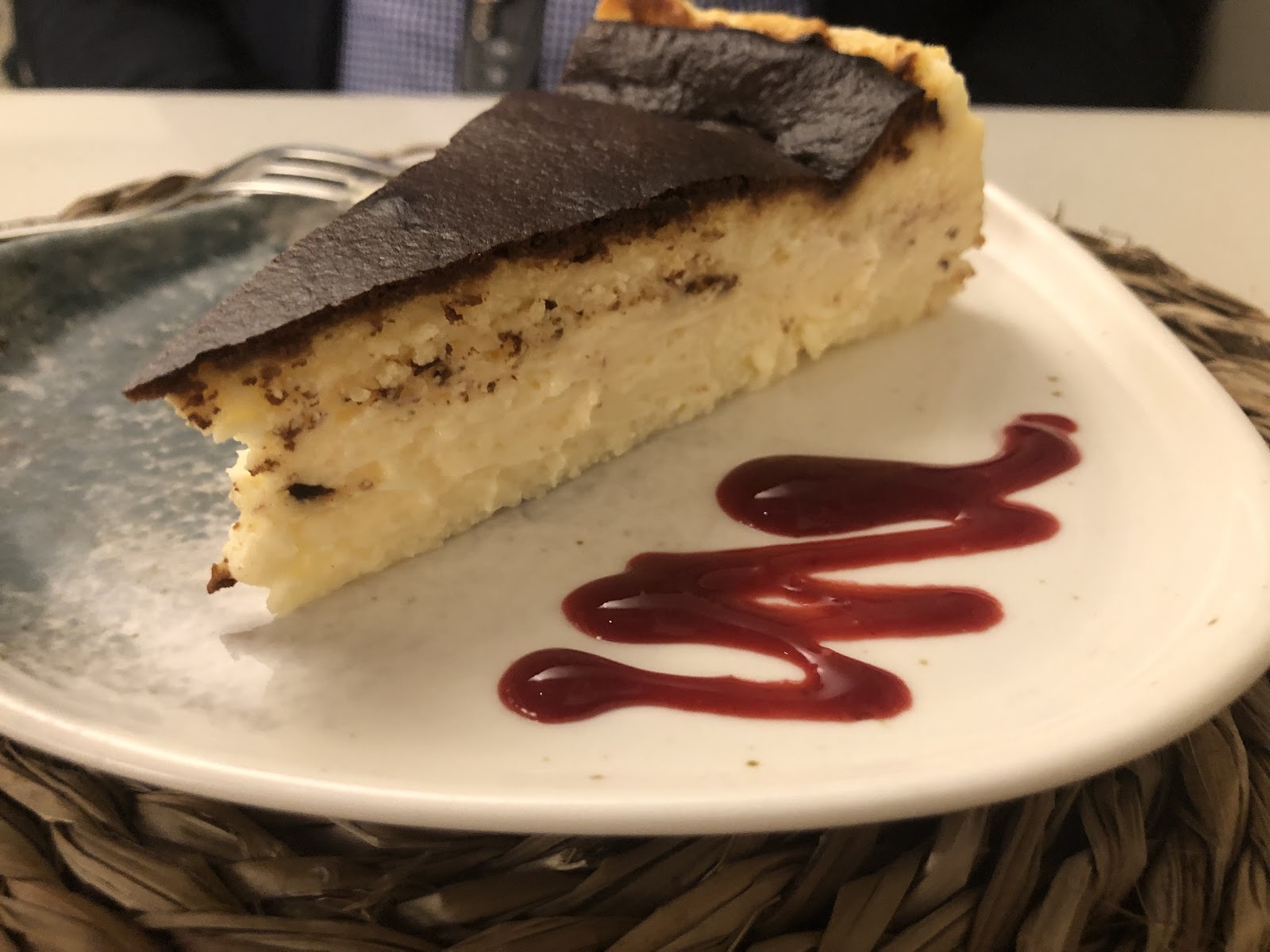 Porción de tarta de queso vasca con la parte superior quemada y coulis de frambuesa