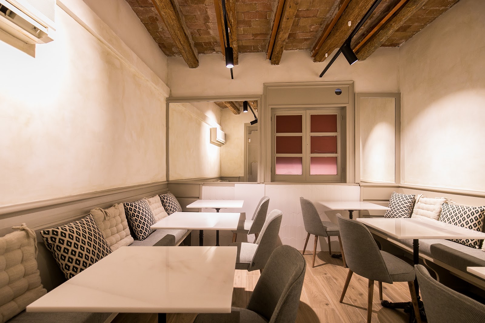 Comedor con asientos de banqueta, mesas blancas y techo con vigas vistas