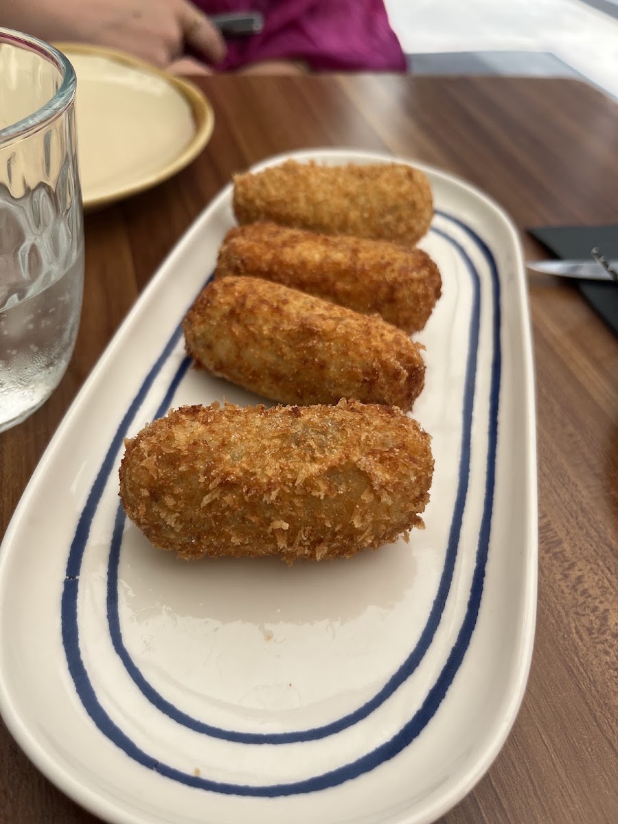 Cuatro croquetas empanadas dispuestas en plato blanco con rayas azules